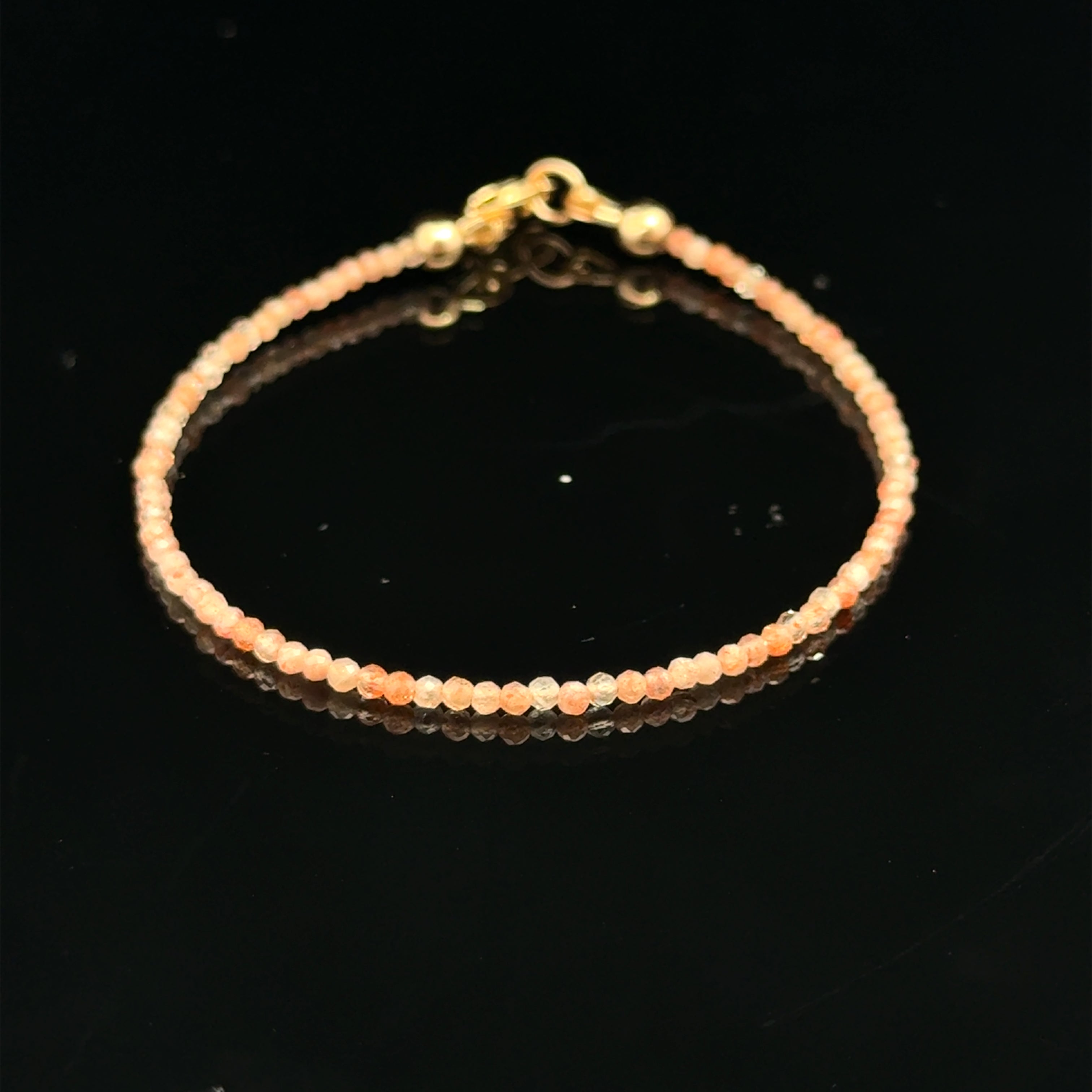 2mm faceted sunstone beaded  bracelet on a black background, front view. 