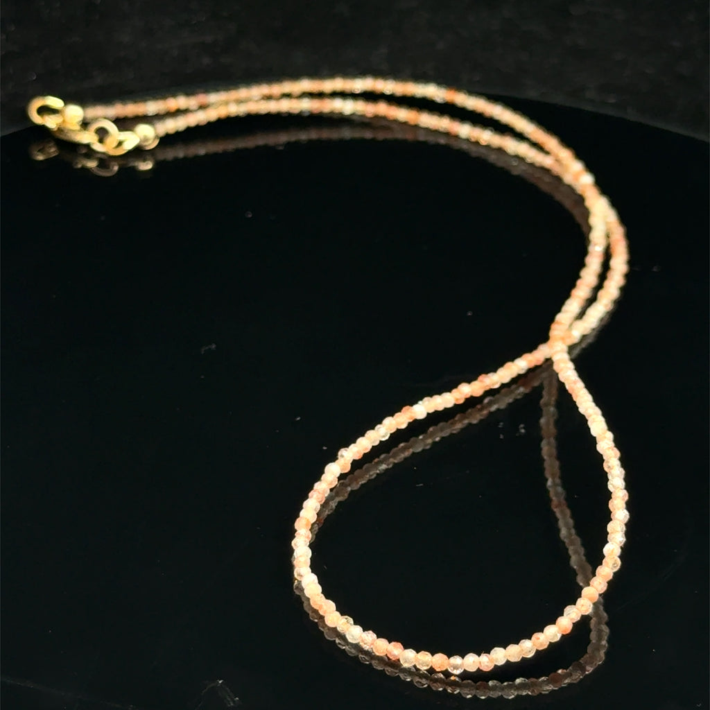2mm faceted sunstone beaded  necklace on a black background, front view. 