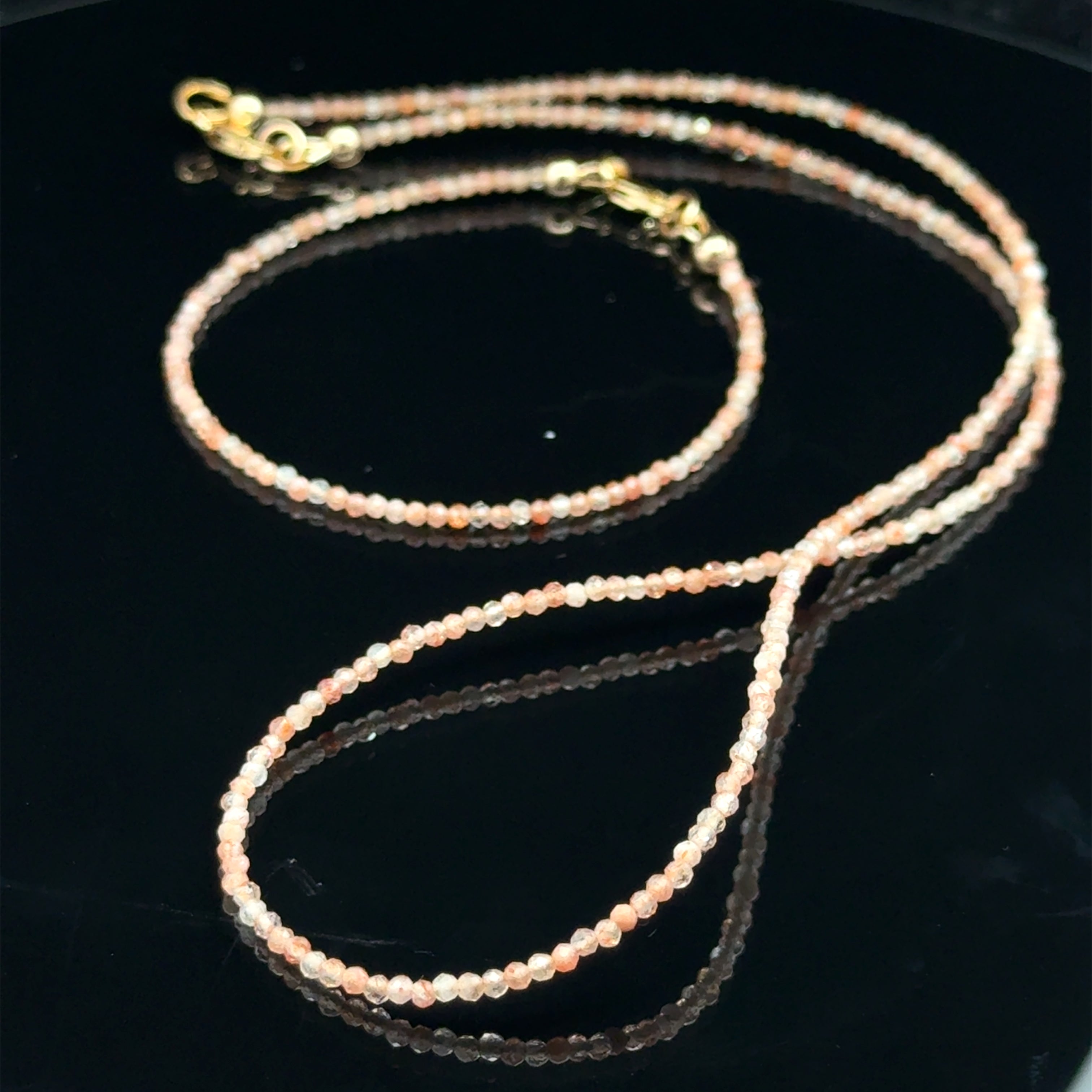 2mm faceted sunstone beaded necklace with gold-filled lobster clasp showing peachy-gold iridescence and aventurescence sparkle with it's matching bracelet on a black background, front view. 
