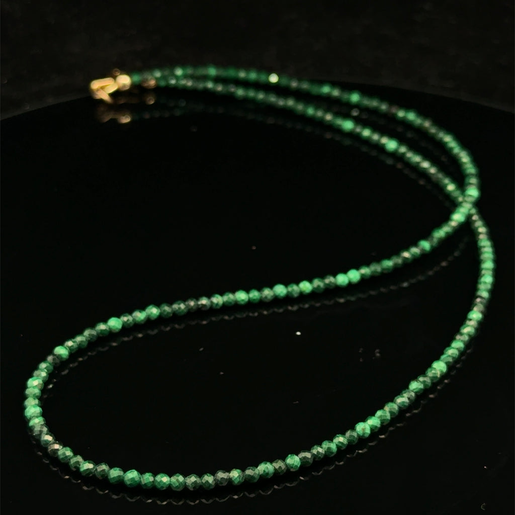 A 2mm faceted round malachite gemstone necklace with gold-filled lobster claw clasp on black background, long overview. 