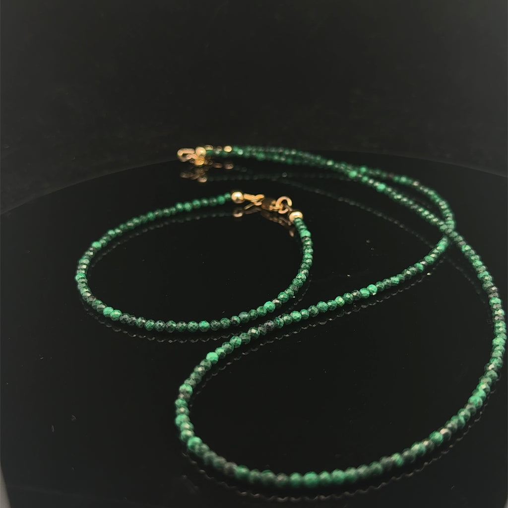 A 2mm faceted round malachite gemstone necklace with gold-filled lobster claw clasp on black background, long overview with it's matching bracelet. 