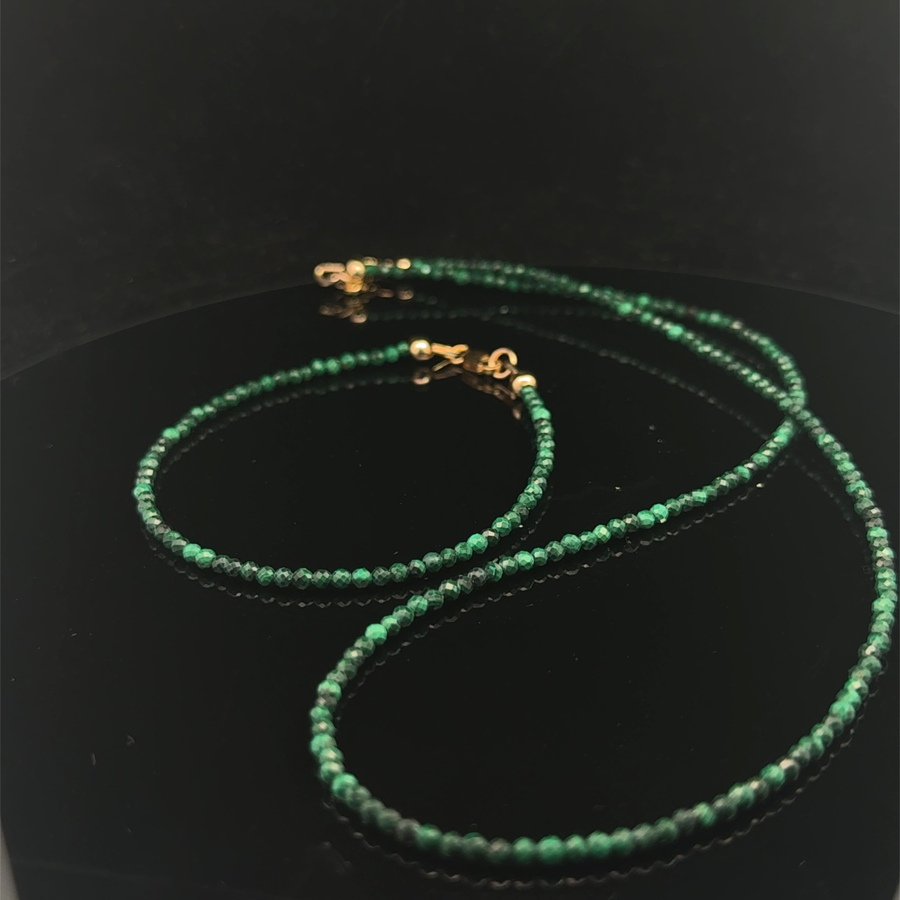 A 2mm faceted round malachite gemstone necklace with gold-filled lobster claw clasp on black background, long overview with it's matching bracelet. 