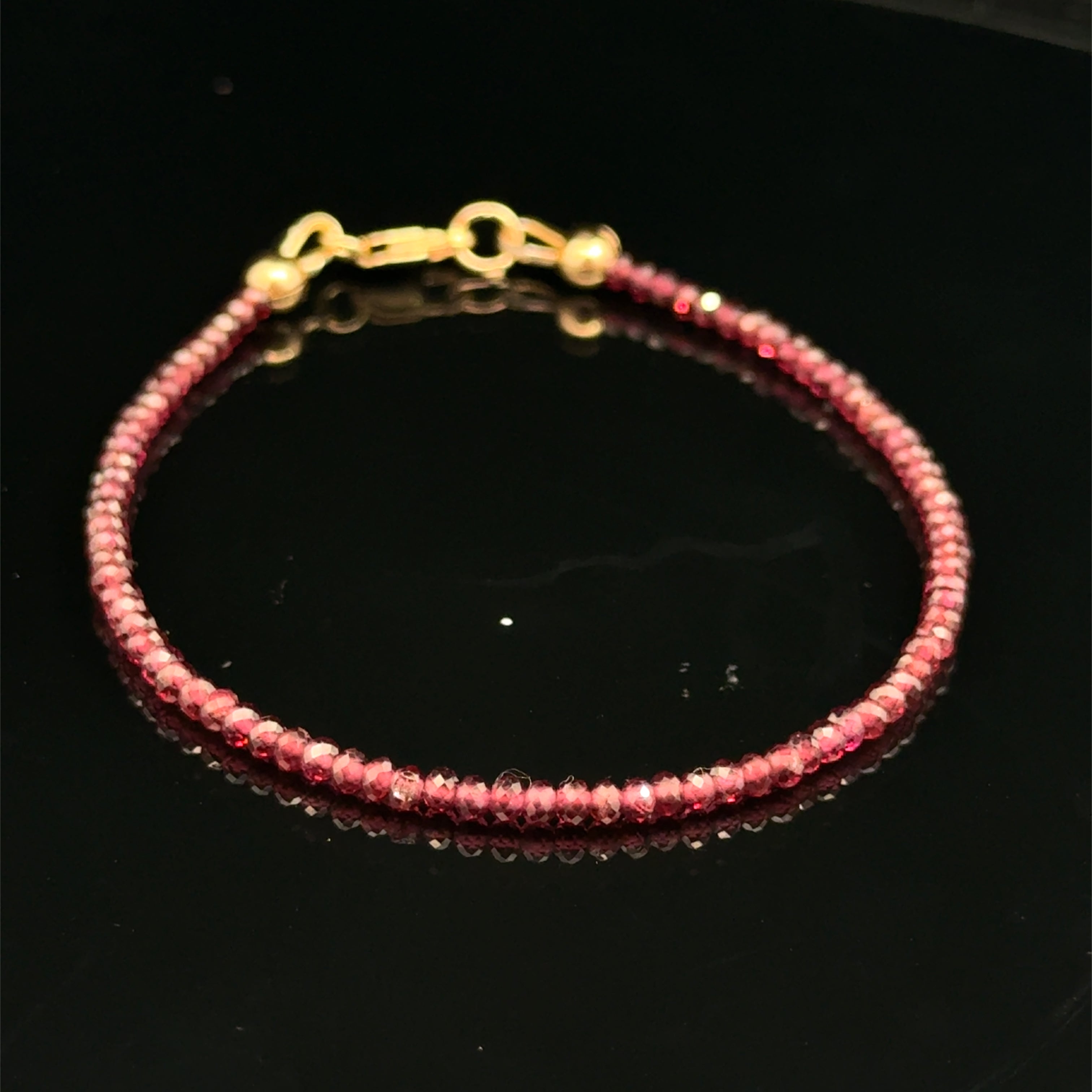 A 2mm faceted roundel red garnet gemstone beaded bracelet with a gold-filled lobster claw on a black background, front overview.