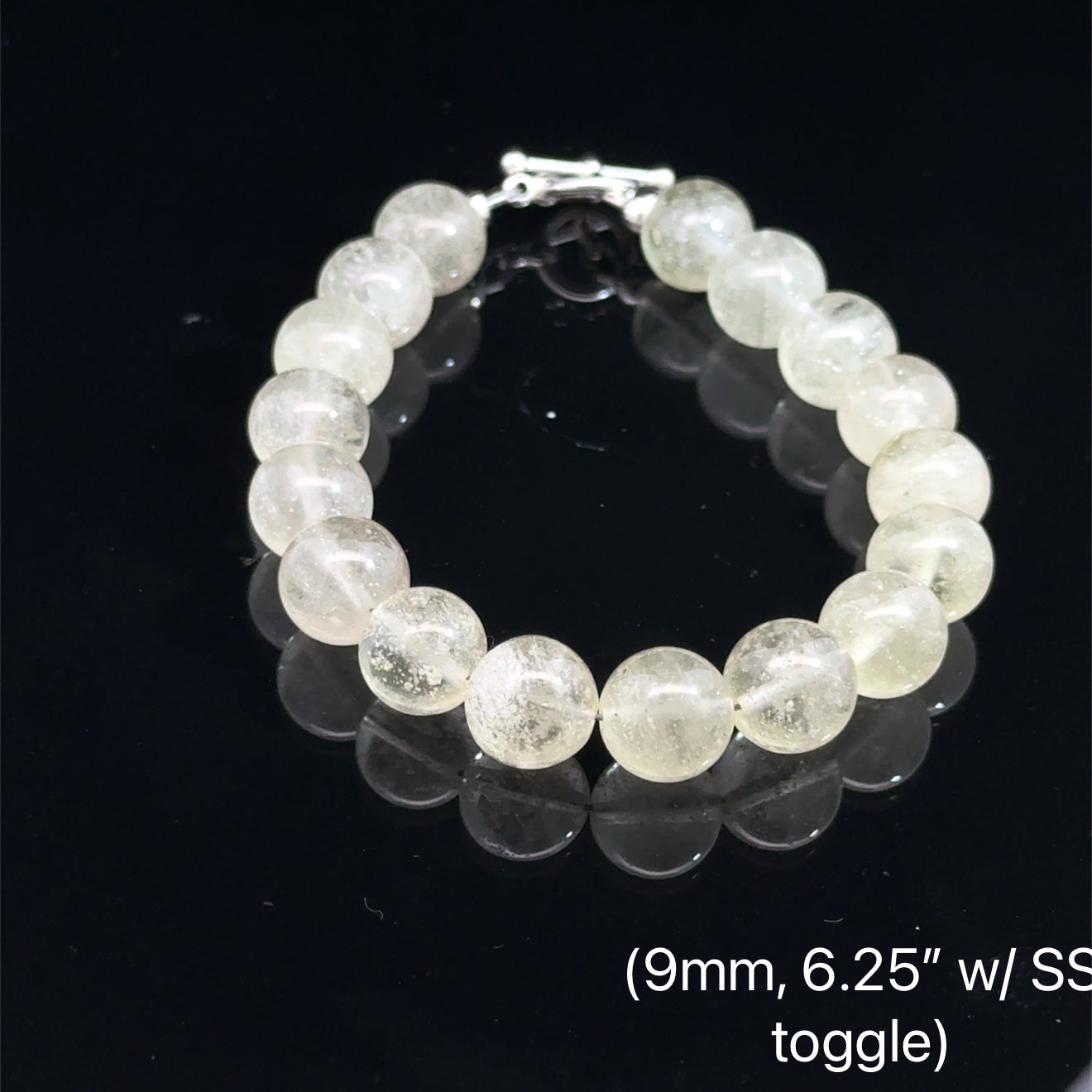 A Close-up of genuine Libyan Desert Glass tektite beads showing translucent golden-yellow color (9mm. 6.25'' w/ sterling silver toggle) on a black background, front overview. 