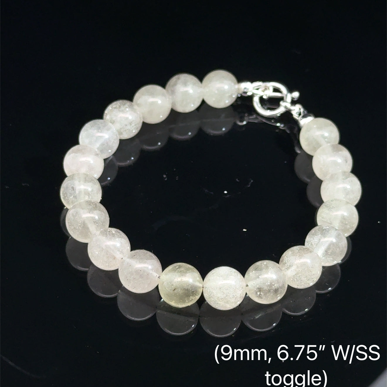 A Close-up of genuine Libyan Desert Glass tektite beads showing translucent golden-yellow color (9mm. 6.75'' w/ sterling silver toggle) on a black background, front overview. 