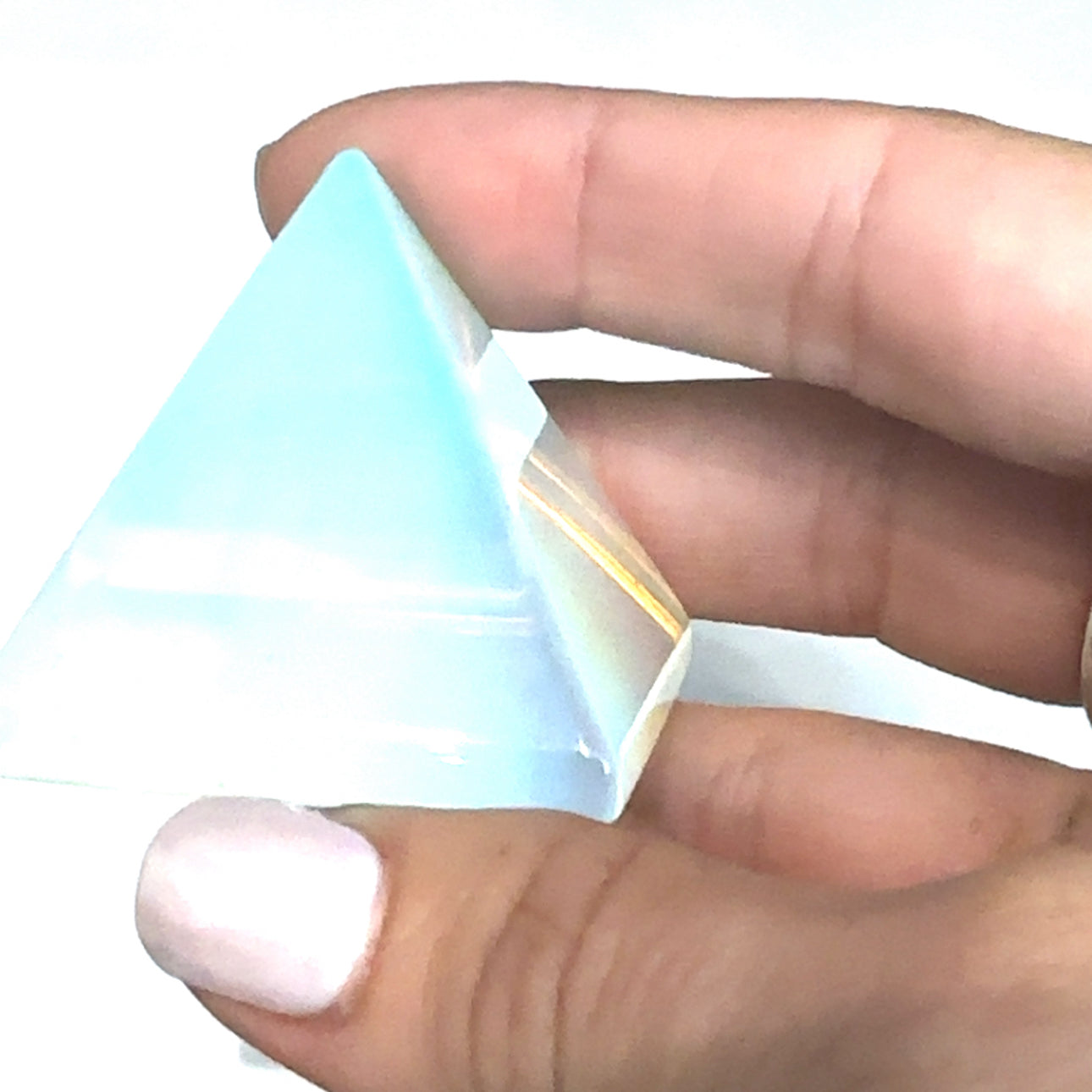 A Opalite Gemstone Pyramid – glowing iridescent crystal for peace and clarity in a models hand on a white background front overview. 