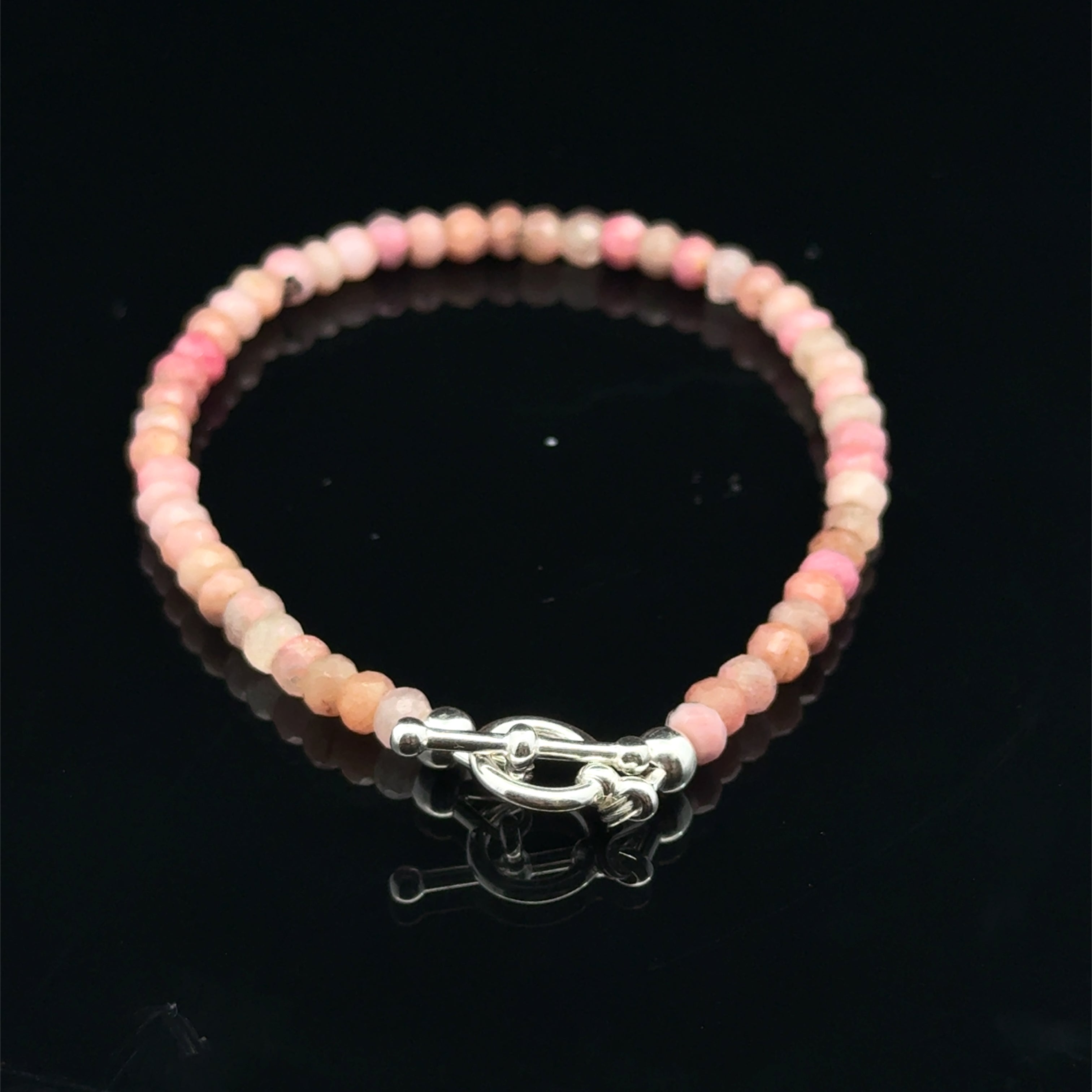 A Rhodochrosite Gemstone 3mm faceted roundel beaded bracelet with a sterling silver toggle, on a black background, back overview.