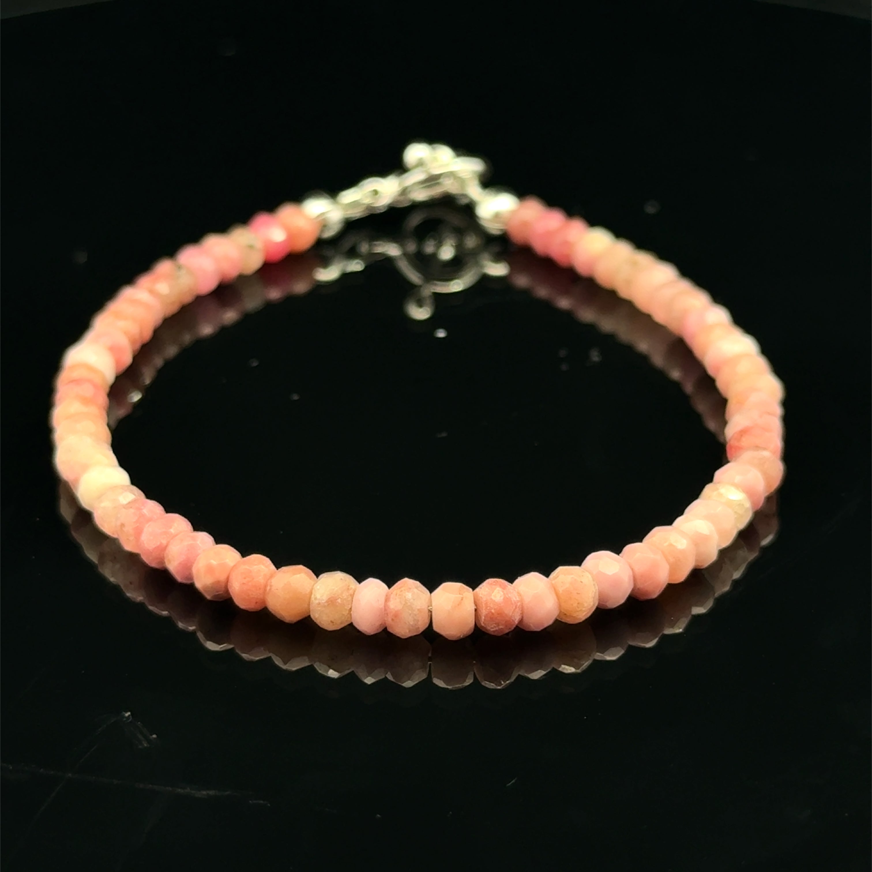 A Rhodochrosite Gemstone 3mm faceted roundel beaded bracelet with a sterling silver toggle, on a black background, front close-up overview.