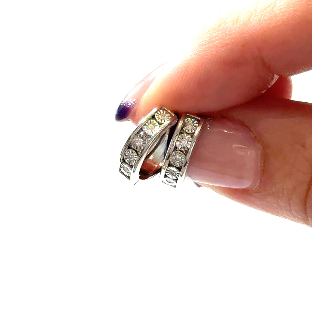 A Sterling Silver .8ct 10 Lab Grown Diamond channel set huggie hoop earrings on a white background, in a models finger tips, front view. 