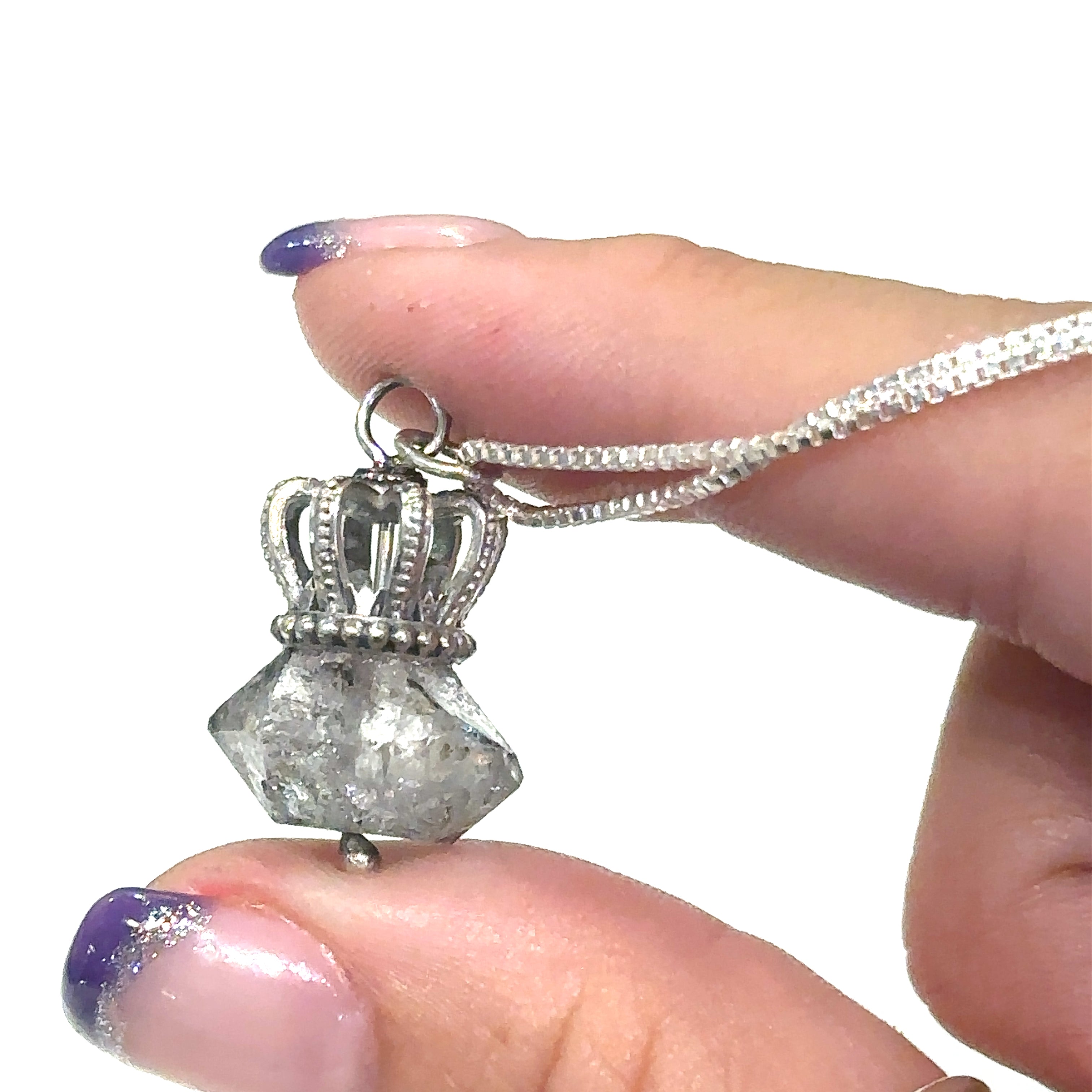 A Sterling Silver Crown Pendant with Herkimer Diamond  gemstone on a white background, in a models finger tips overview.  