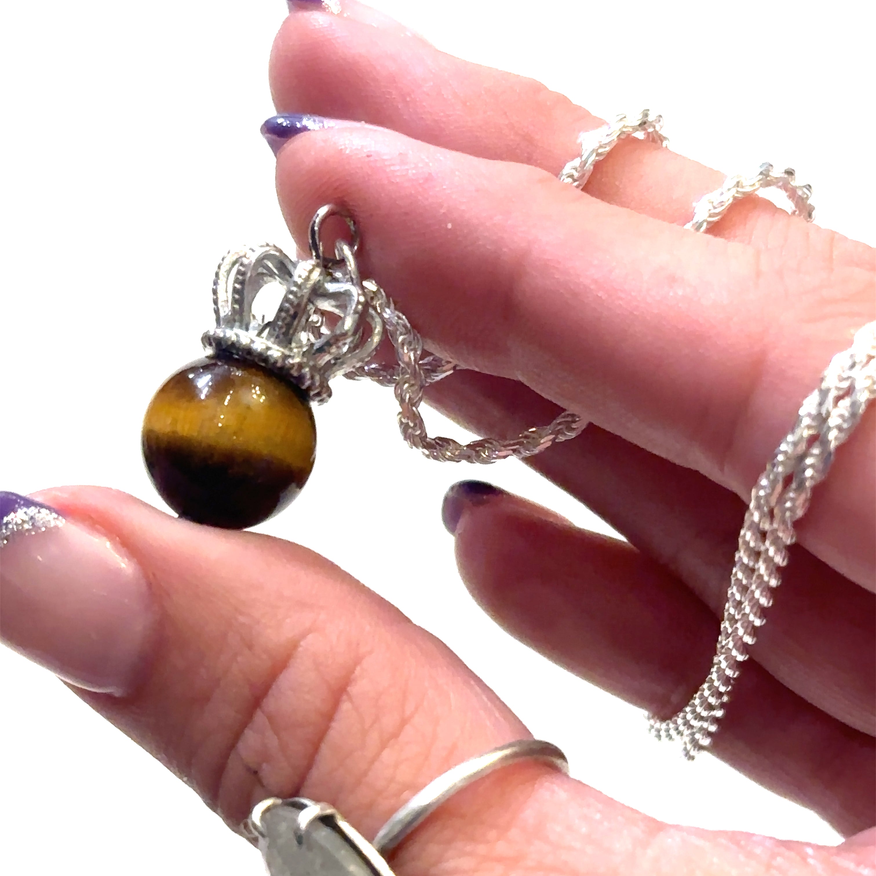A Sterling Silver Crown Pendant with golden tiger eye gemstone on a white background, in a models finger tips.  
