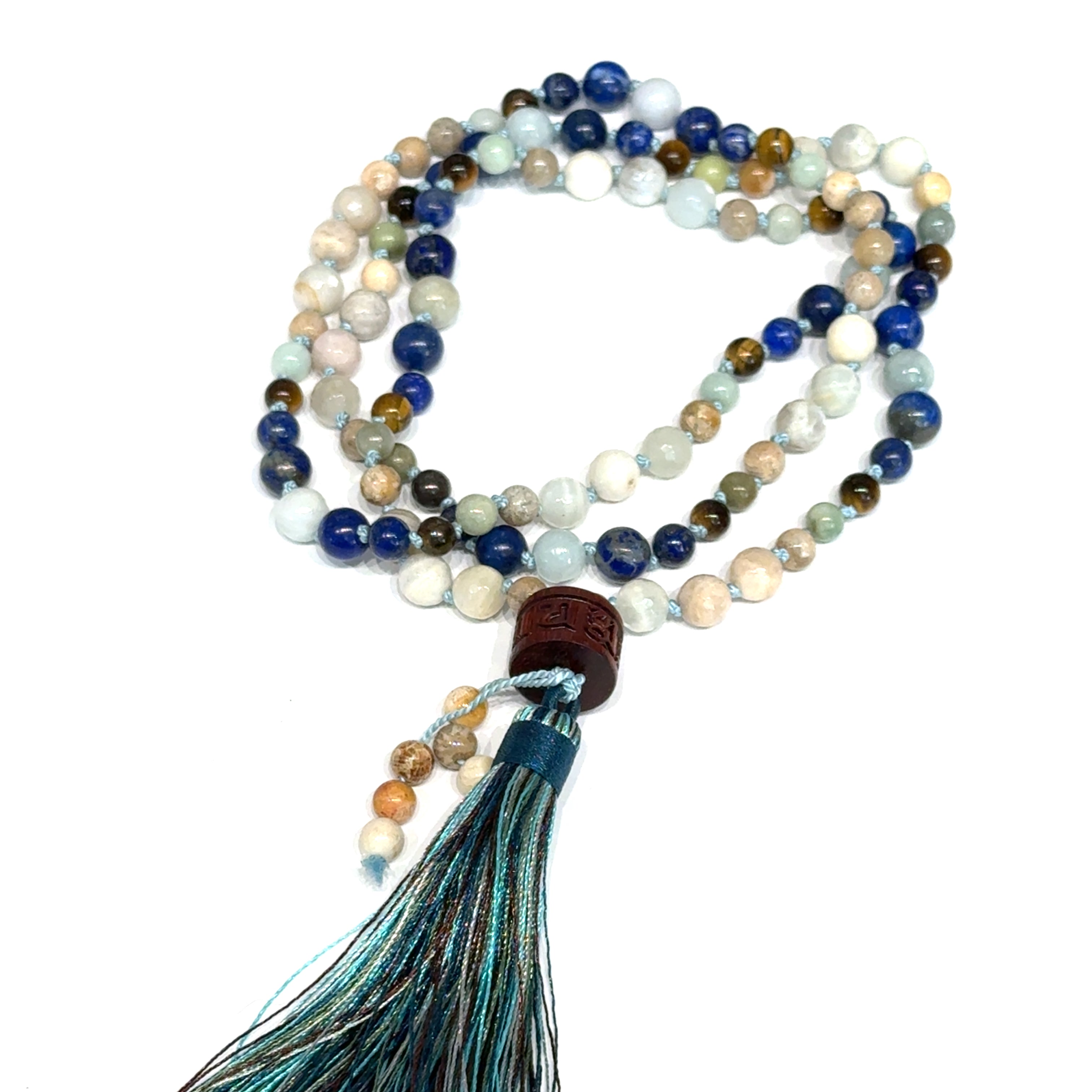 A beaded gemstone Mala necklace with a variety of colors, including blue, white, and brown, featuring a tassel end, on a white background, center, circle, close-up overview. 