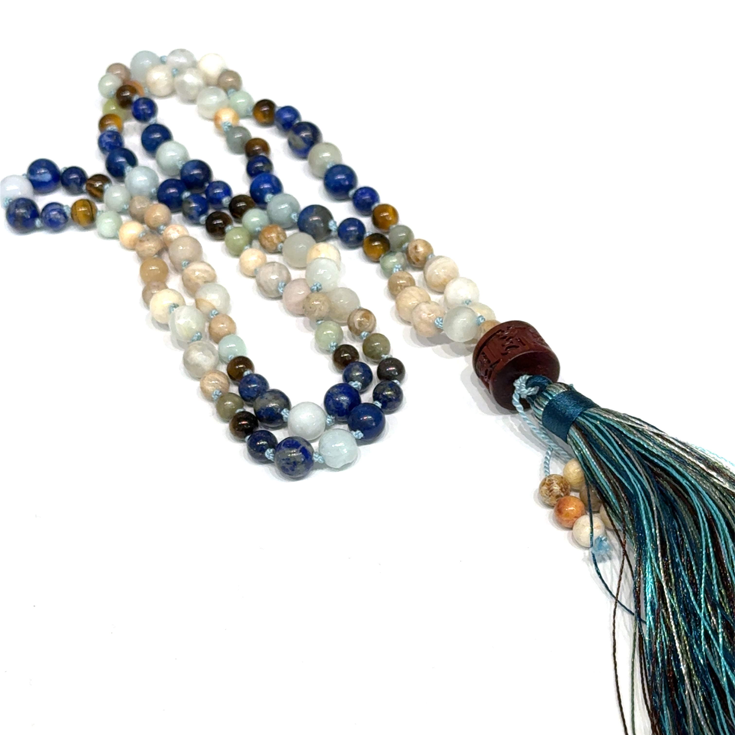 A beaded gemstone Mala necklace with a variety of colors, including blue, white, and brown, featuring a tassel end, on a white background, center, long, close-up overview. 