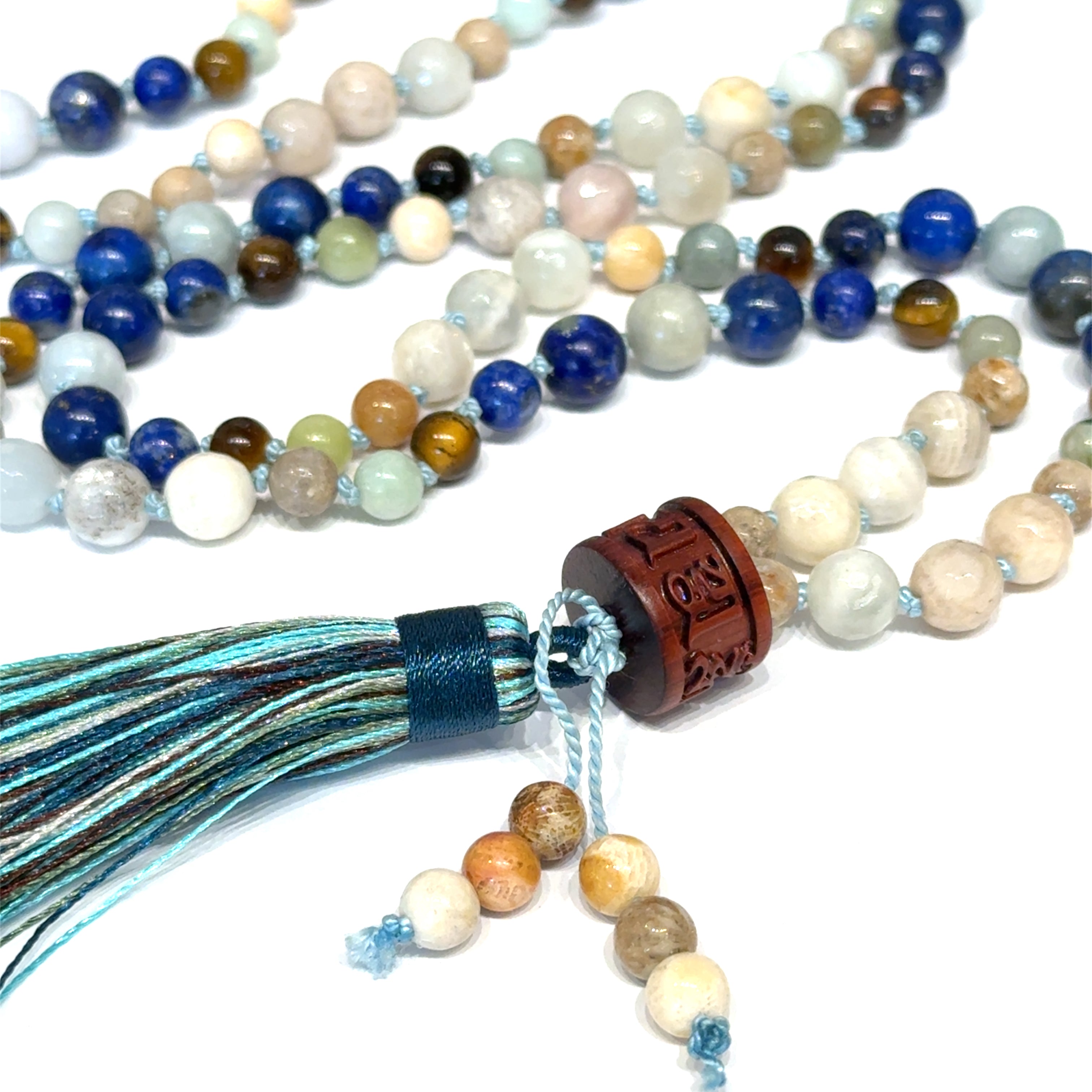 A beaded gemstone Mala necklace with a variety of colors, including blue, white, and brown, featuring a tassel end, on a white background, close-up overview. 