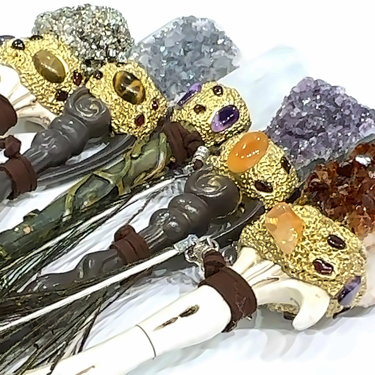 A collection of gemstone wands with various colored gemstones, each topped with a different decorative element, such as peacock feathers or charms, on a white background. 