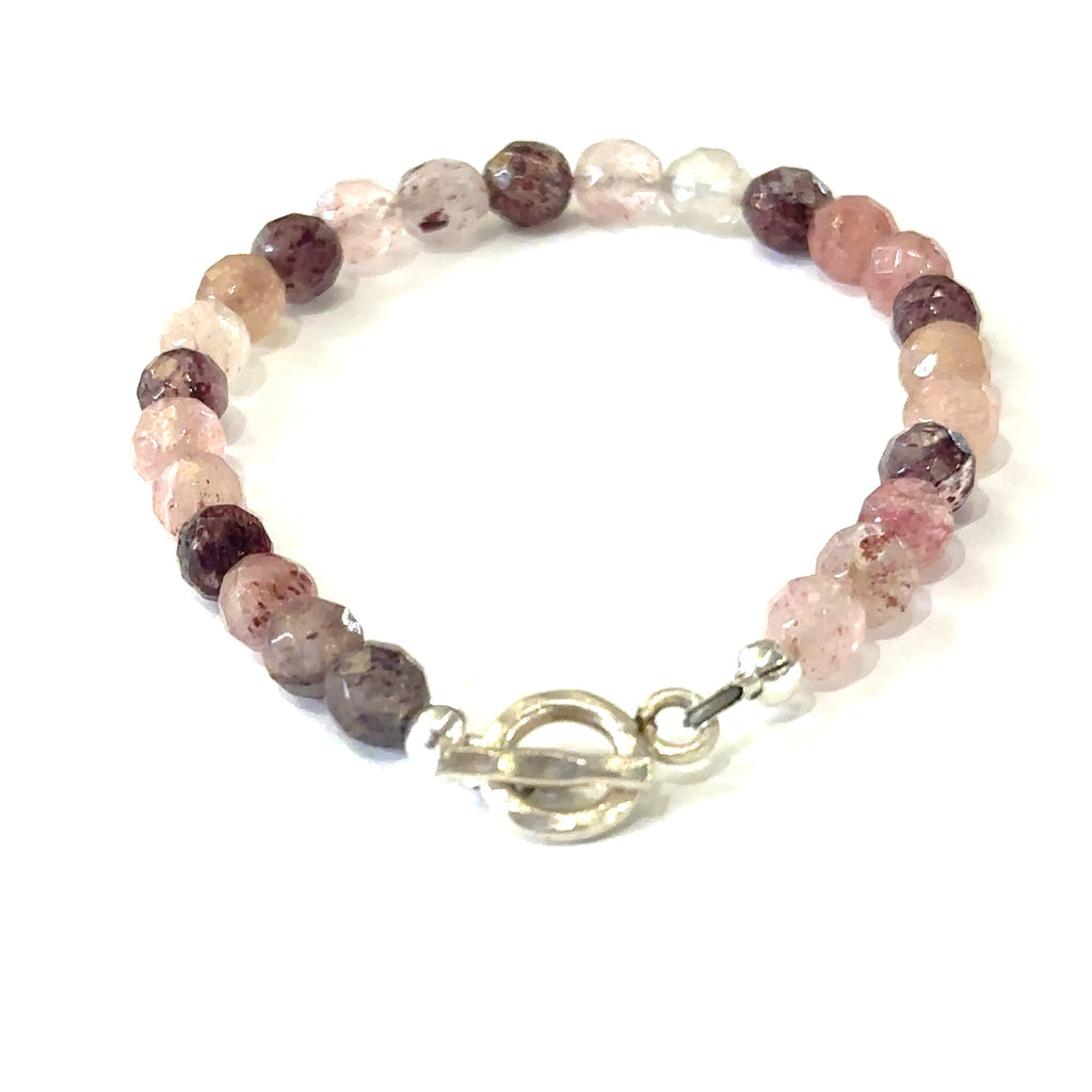 A genuine Strawberry Quartz gemstone bracelet with faceted beads and a aterling silver toggle on a white background, with a center back overview. 