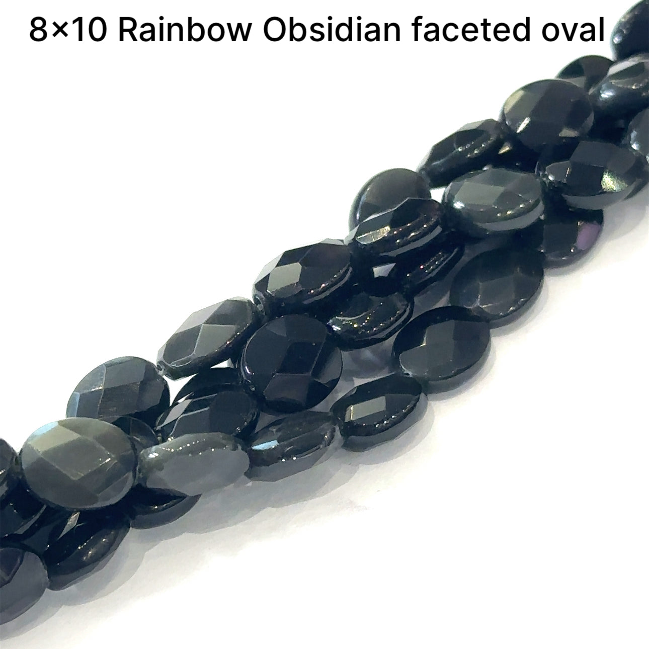 A group of strands of 8x10mm Rainbow Obsidian faceted oval gemstone beads on a white background, front overview. 