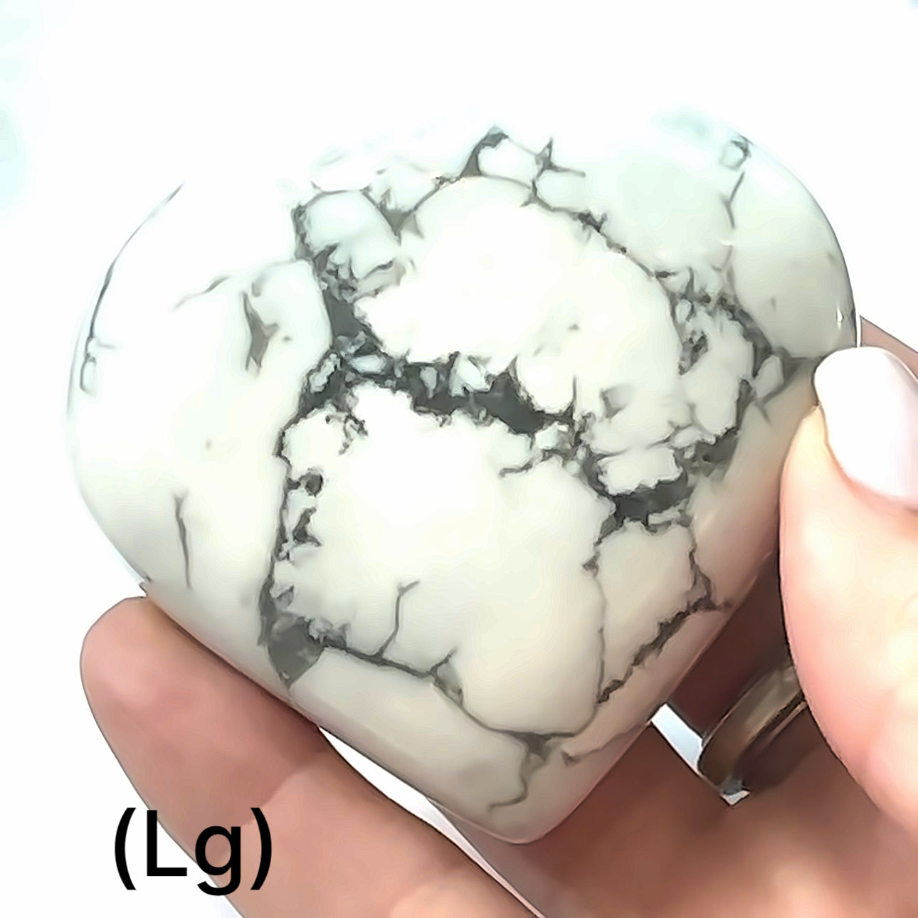 A hand holding a heart-shaped Howlite gemstone with a white and gray marbled pattern, size large, on a white background, front view.