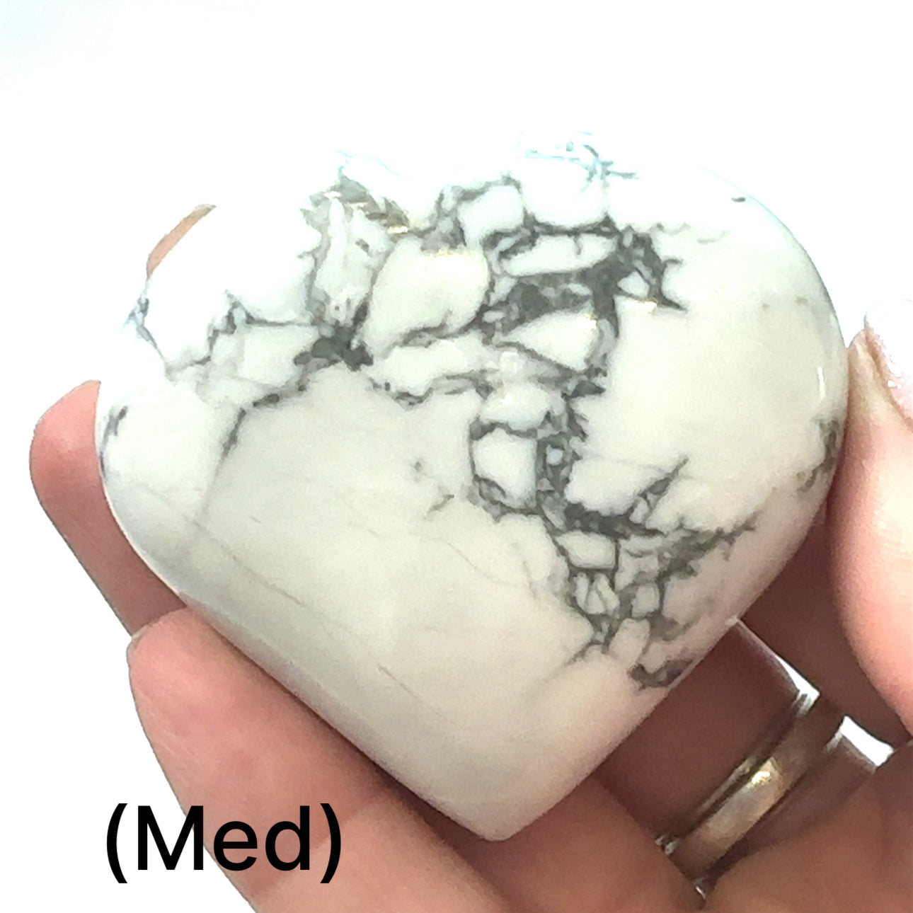 A hand holding a heart-shaped Howlite gemstone with a white and gray marbled pattern, size medium, on a white background, front view.