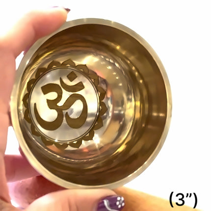 A hand holding a small, round, golden Himalayan singing bowl with an interior design, placed against a white background. The bowl is 3 inches in diameter. front view