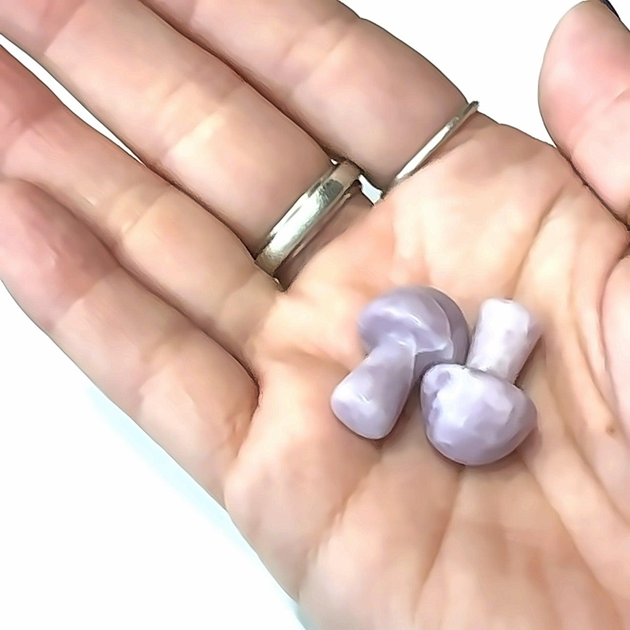 A hand holding several Kunzite mini mushroom-shaped gemstone carvings on a white background, front view. 