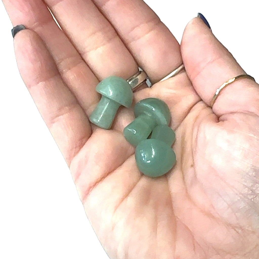 A hand holding several green averturine mini mushroom-shaped gemstone carvings on a white background, front view. 