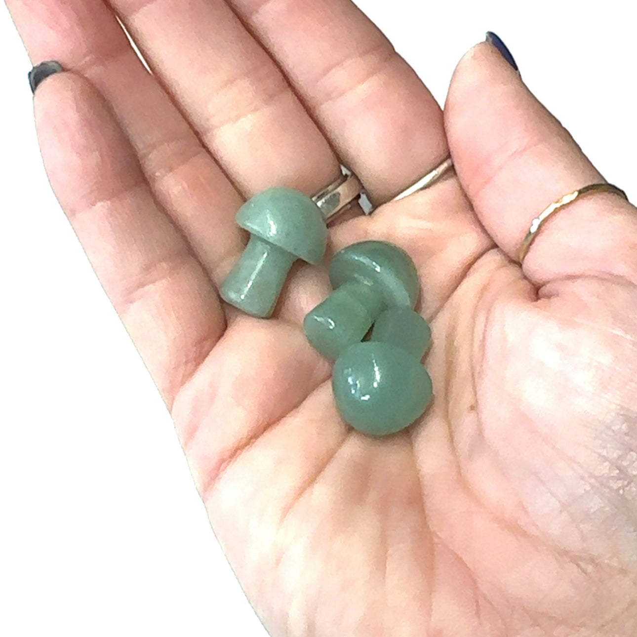 A hand holding several green averturine mini mushroom-shaped gemstone carvings on a white background, front view. 