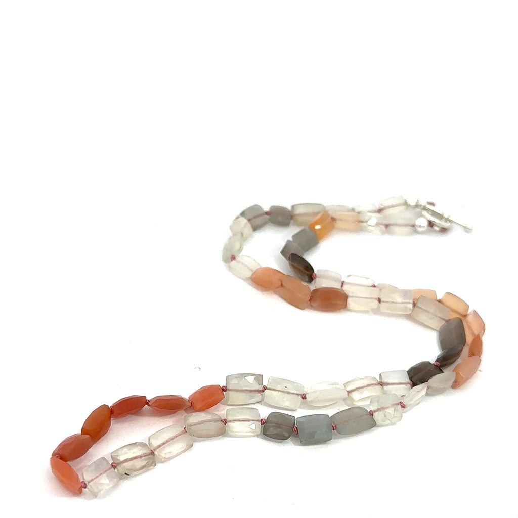 A knotted necklace made of mixed moonstone gemstones with a sterling silver toggle clasp on a white background, long overview close up.