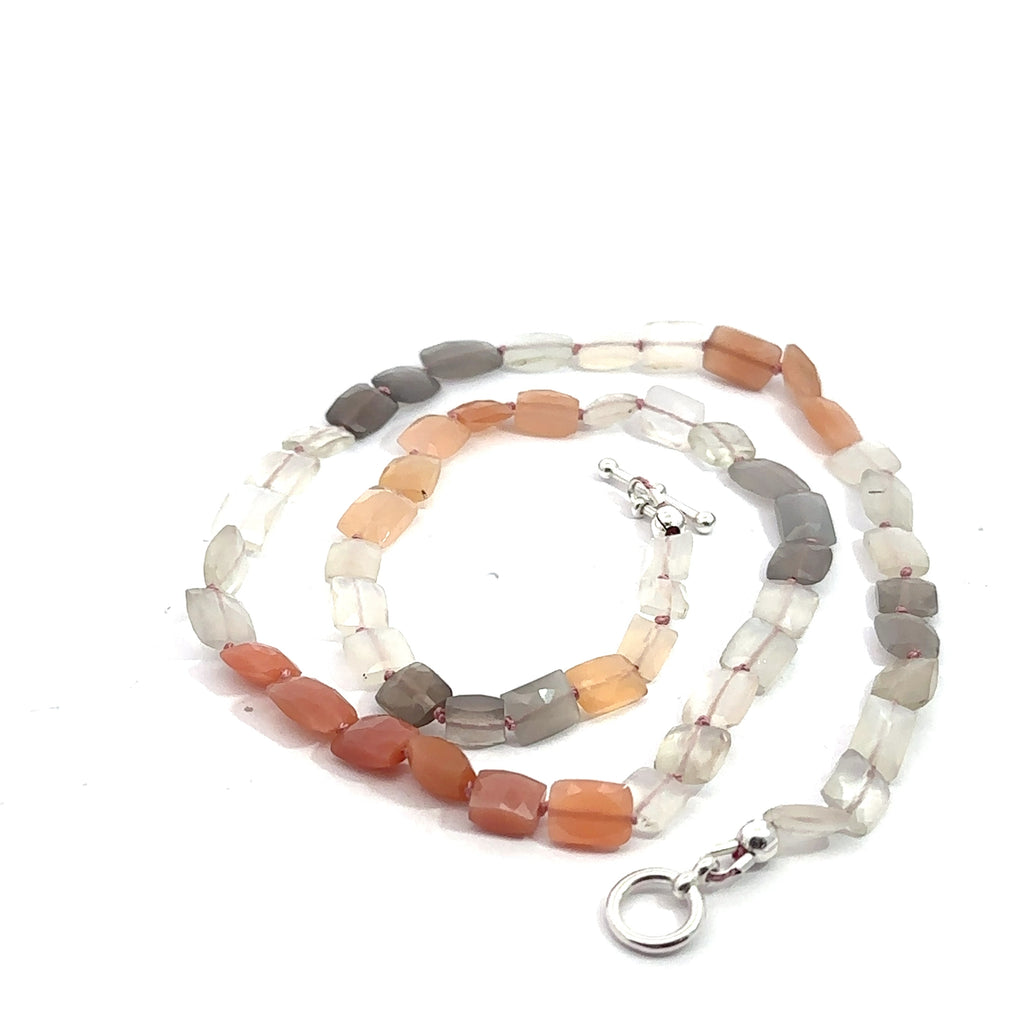 A knotted necklace made of mixed moonstone gemstones with a sterling silver toggle clasp on a white background, spiral overview. 