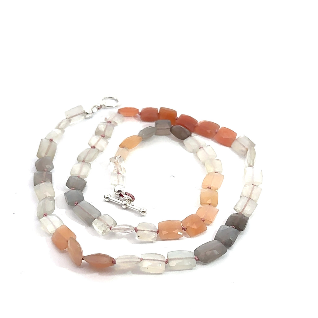 A knotted necklace made of mixed moonstone gemstones with a sterling silver toggle clasp on a white background, spiral overview close up.