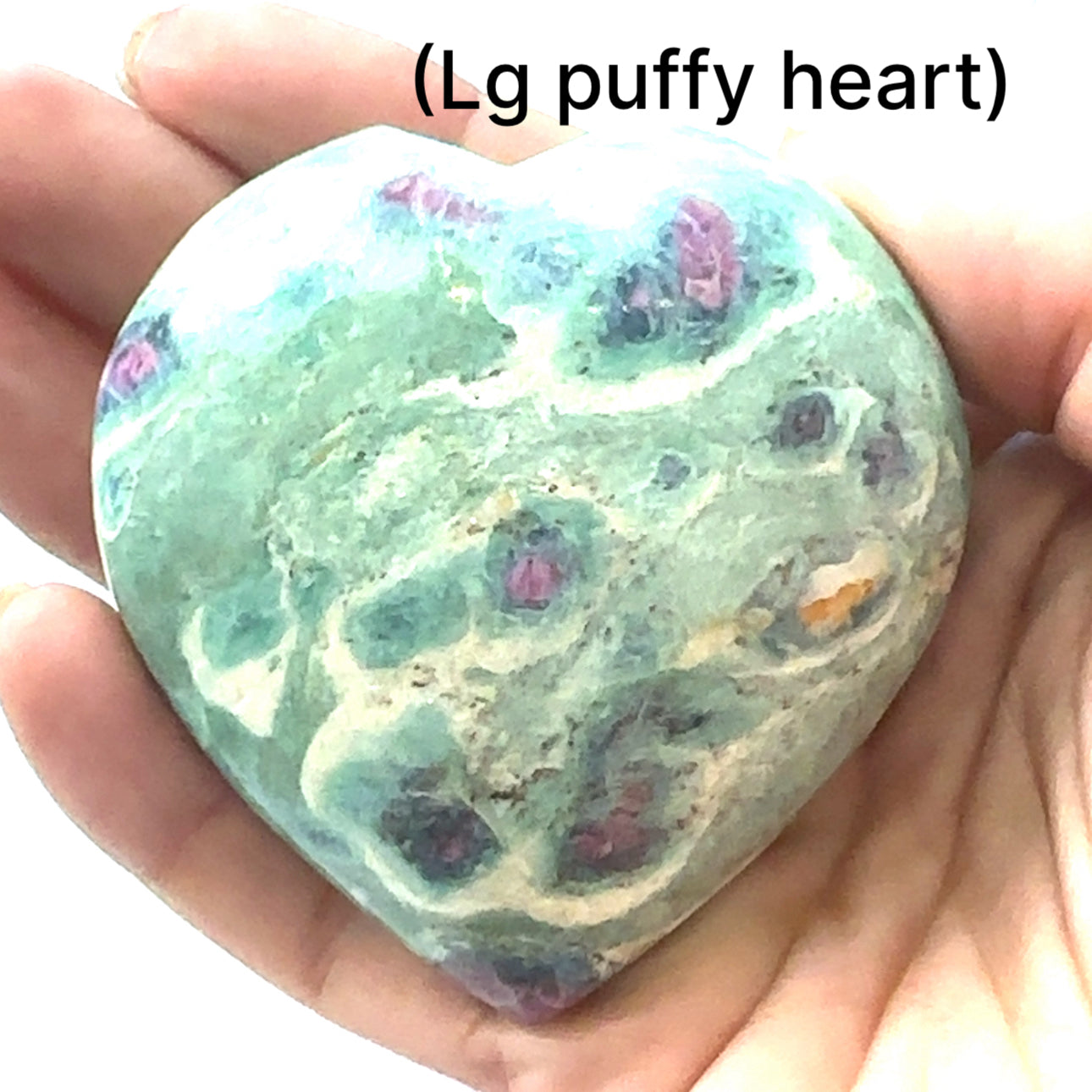 A large puffy heart-shaped Ruby Fuchsite gemstone carvings displayed in a models hand on a white background front overview.