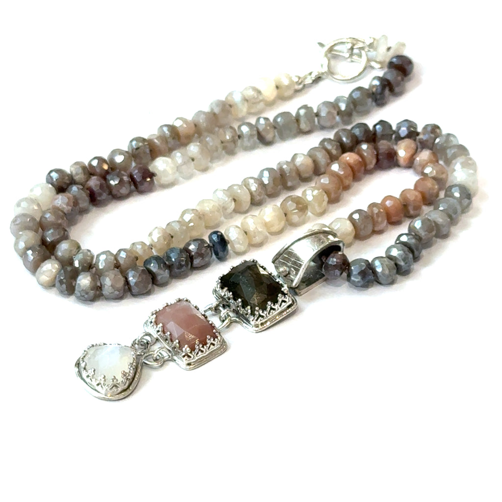 A mixed moonstone faceted roundel knotted necklace with a custom forged sterling silver with three gemstones pendant. on a white background, front center diagonal  overview. 