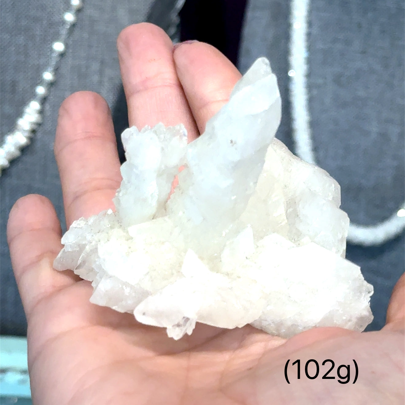 A model holding raw white aragonite specimen gemstones in their hand sizes (102g) on a mixed-colored background, front view.