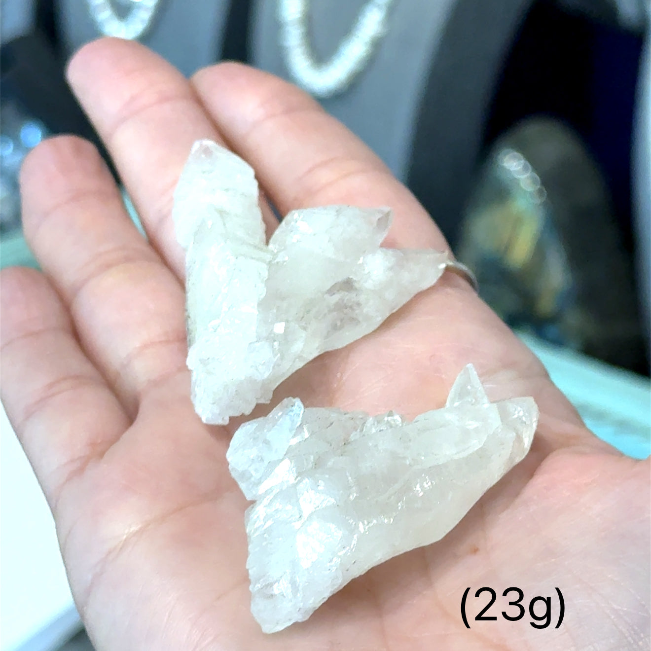 A model holding raw white aragonite specimen gemstones in their hand sizes (23g) on a mixed-colored background, front view.