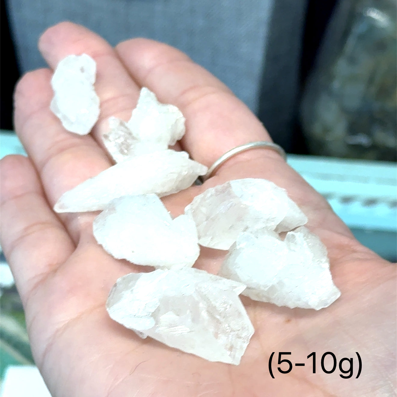 A model holding raw white aragonite specimen gemstones in their hand sizes (5-10g) on a mixed-colored background, front view.