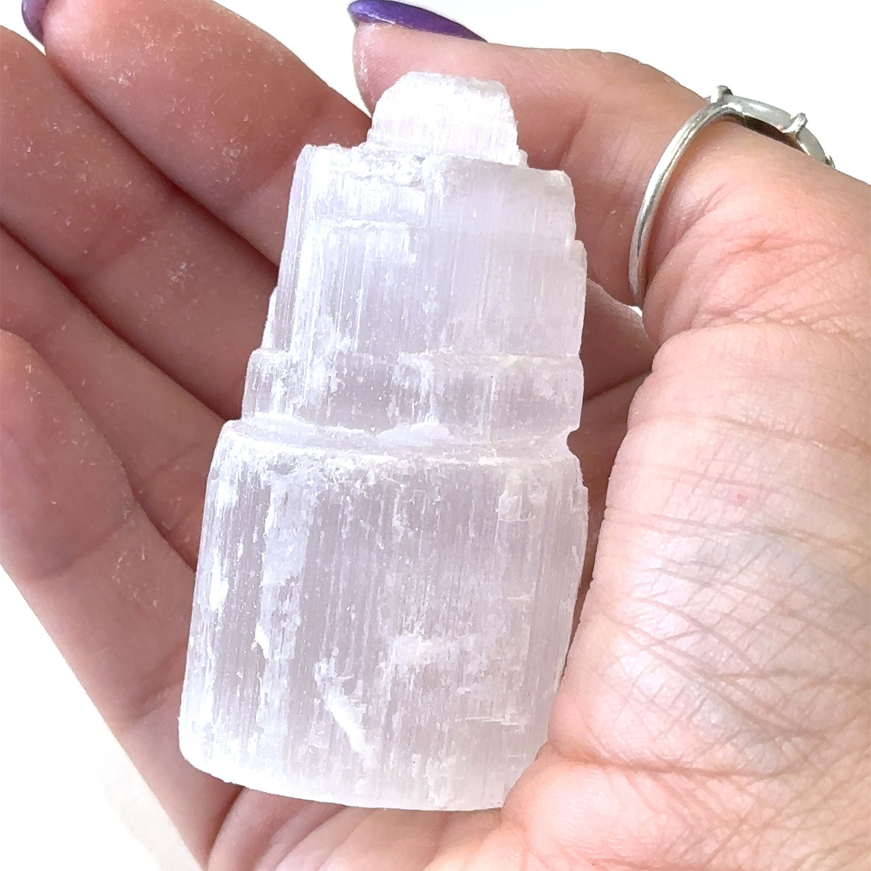 A selenite gemstone raw towers displayed in a models palm on a white background, front close up overview. 