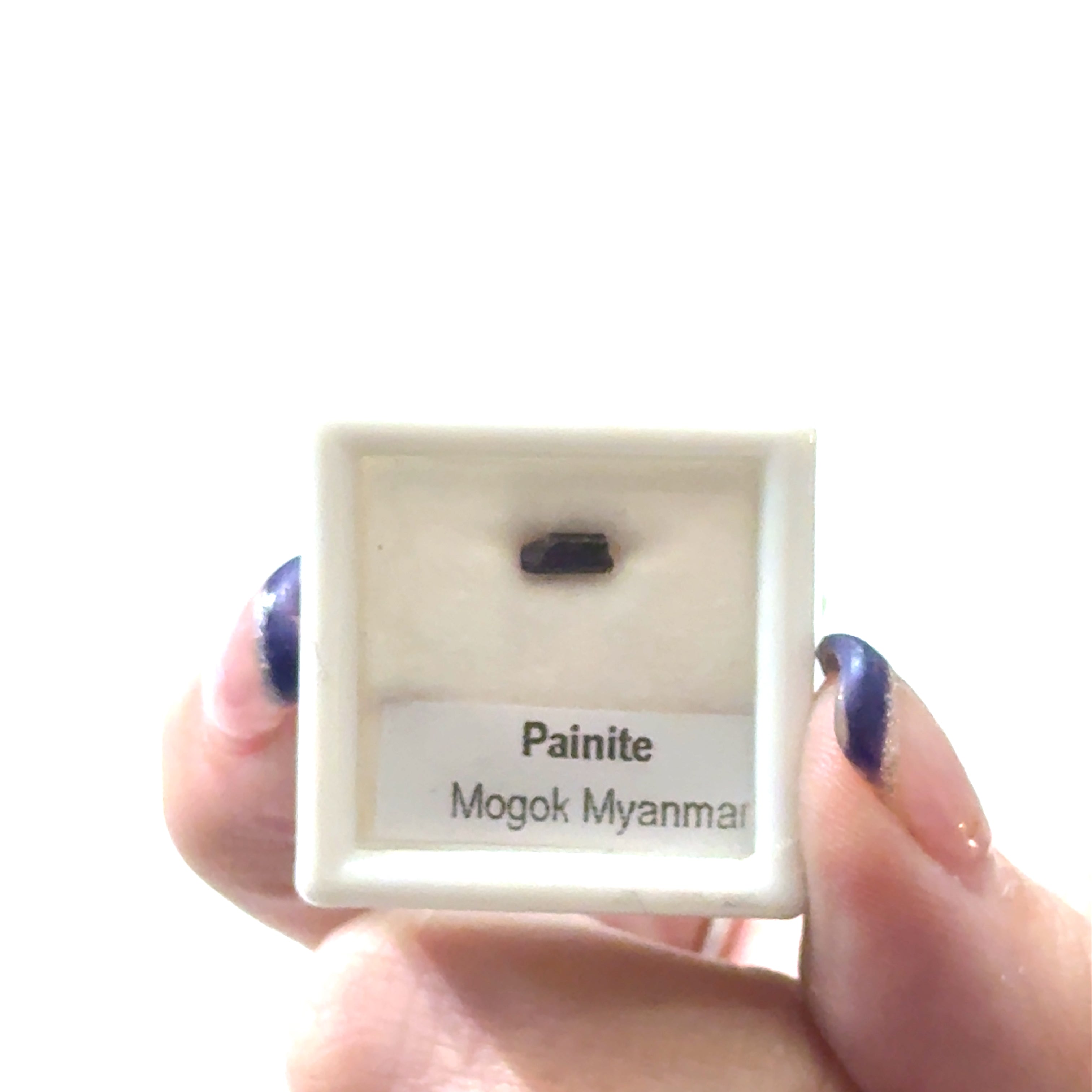 A small gemstone in a display case with 'Painite Mogok Myanmar' label and weighing  .30ct  on a white background front view. 