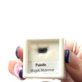 A small gemstone in a display case with 'Painite Mogok Myanmar' label and weighing  .60ct  on a white background front view. 