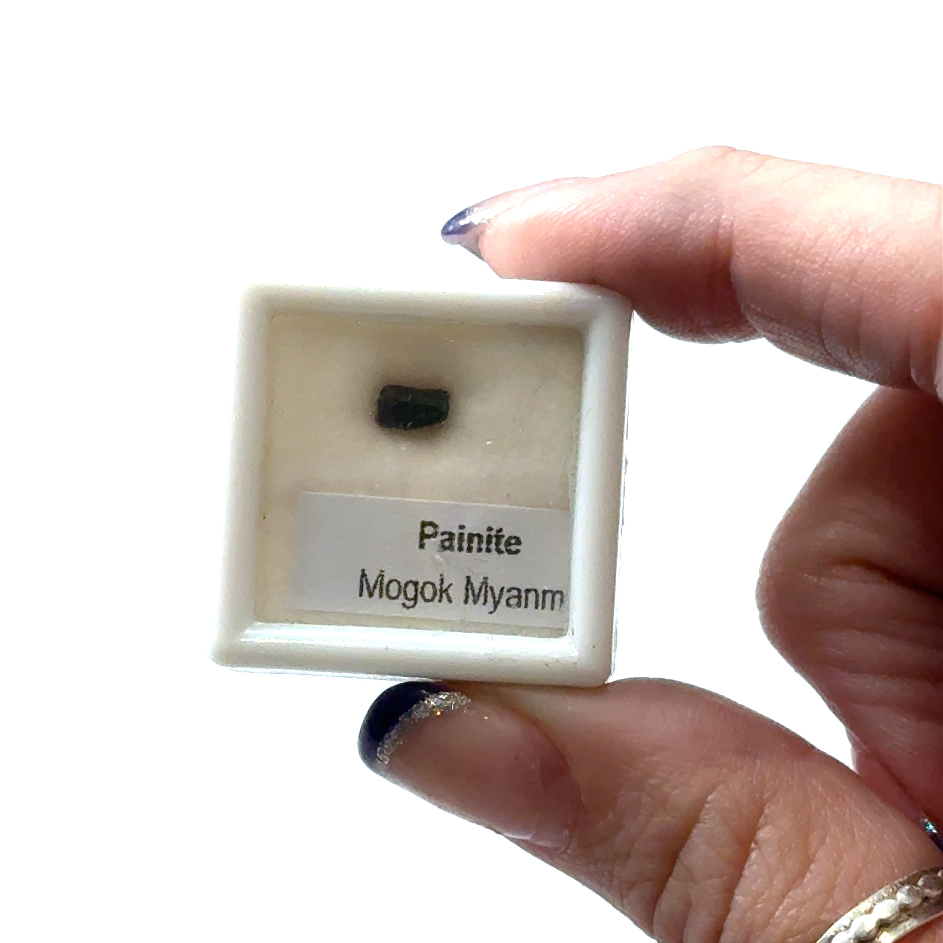 A small gemstone in a display case with 'Painite Mogok Myanmar' label and weighing  .65ct  on a white background front view. 
