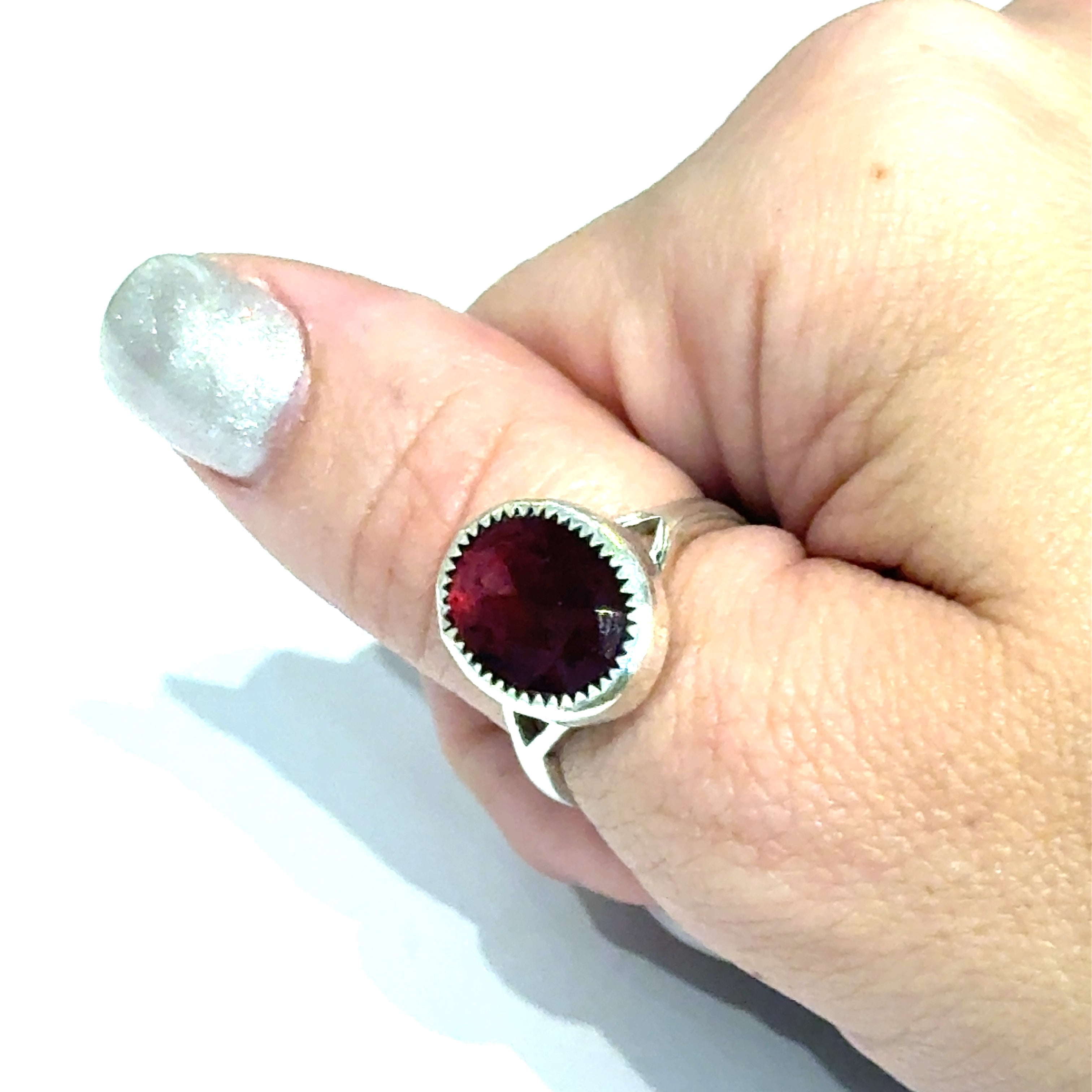 Almandine Garnet gemstone sterling silver ring in a model's thumb on a white background, front view. 