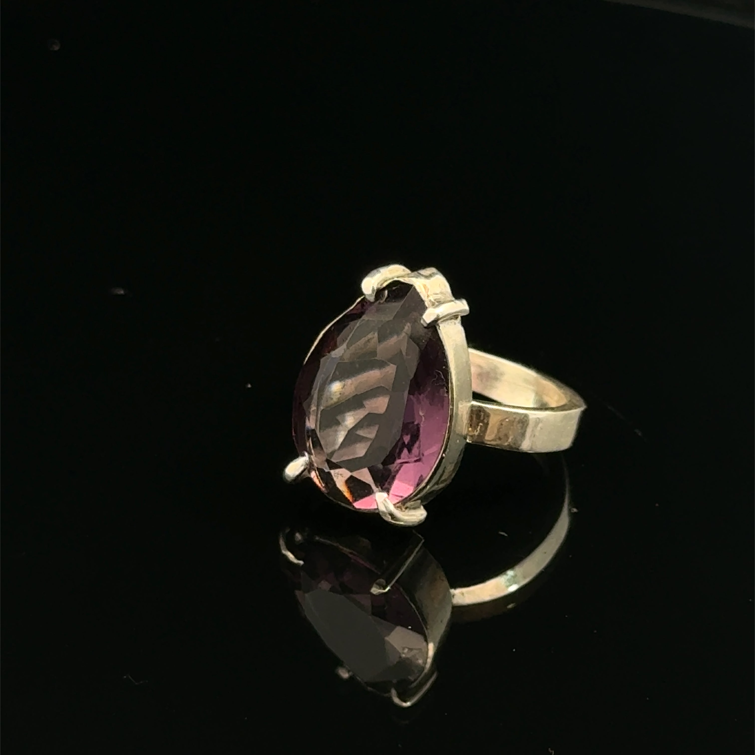 An Ametrine Ring with a purple teardrop-shaped gemstone on a  black  background, left side front view.
