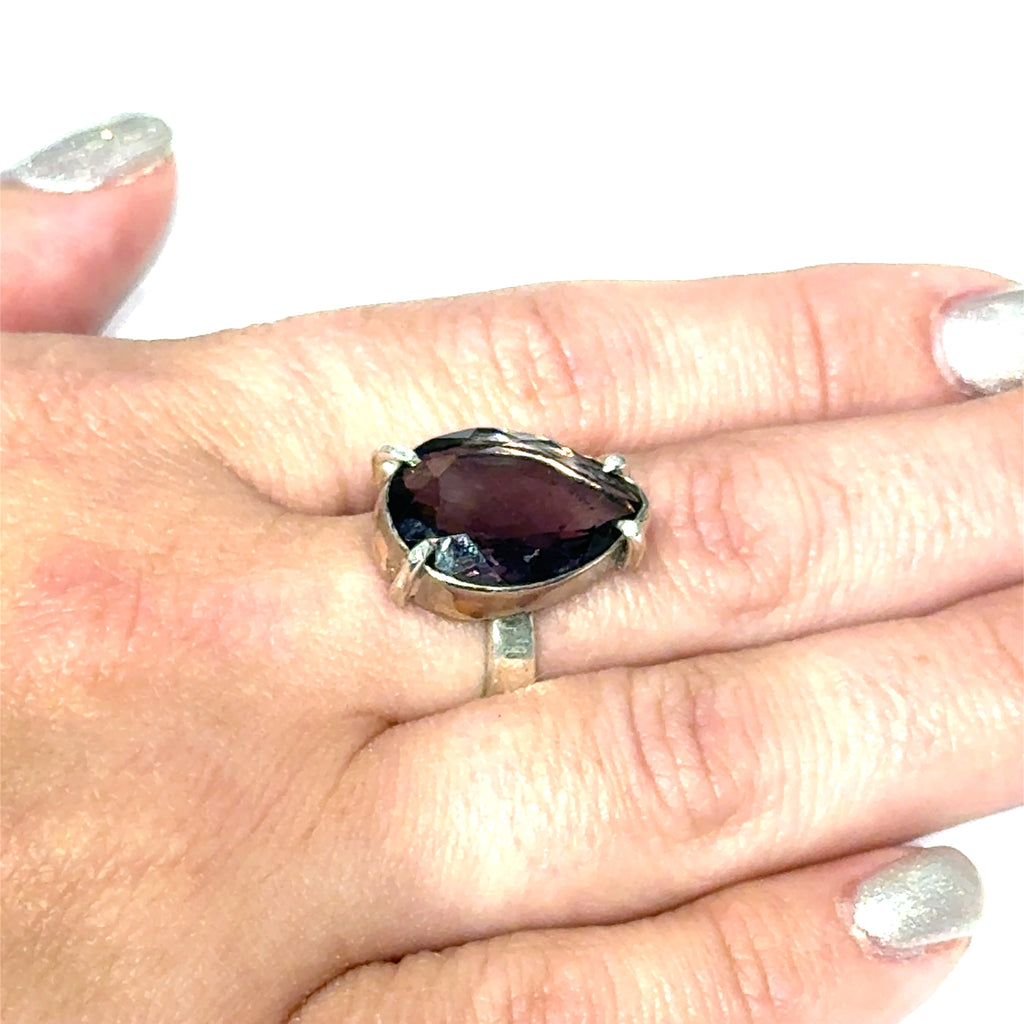 An Ametrine Ring with a purple teardrop-shaped gemstone on a models finger on a white background, front close up view.