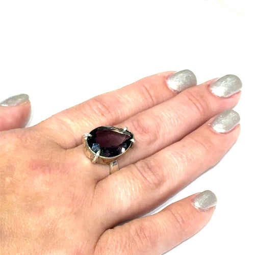 An Ametrine Ring with a purple teardrop-shaped gemstone on a models finger on a white background, front view.