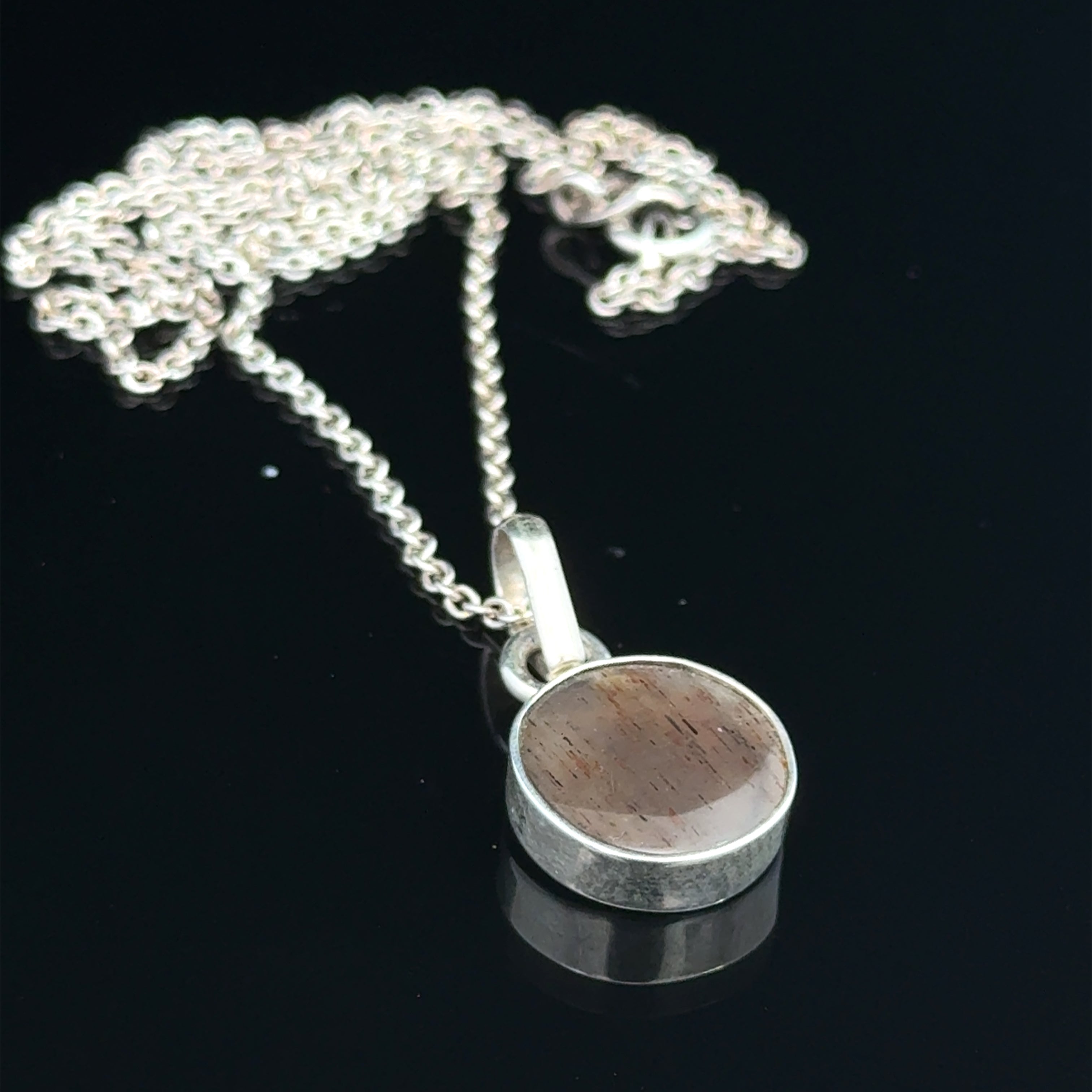 Brown Confetti Moonstone Sunstone pendant set in sterling silver bezel on a black background, hung, front overview. 