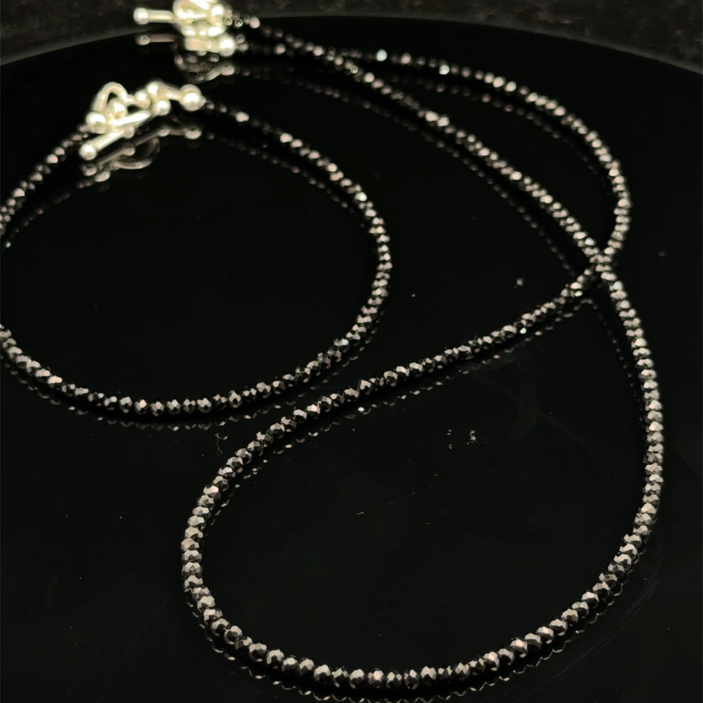 Close-up of Black Spinel beads showing deep black color and brilliant luster, gemstone-quality bracelet for power and protection, on a black background, front side view with its matching necklace.