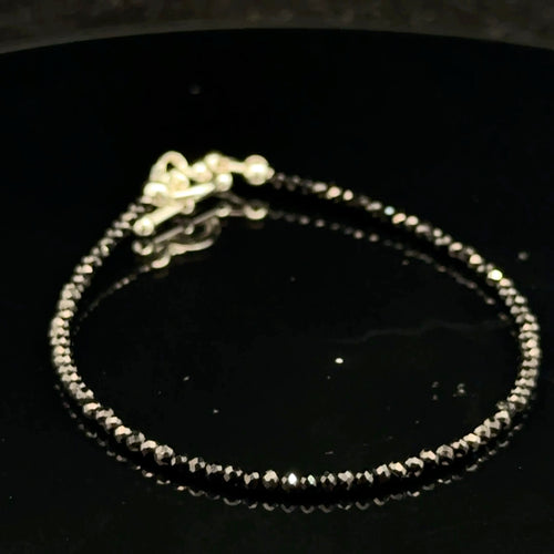 Close-up of Black Spinel beads showing deep black color and brilliant luster, gemstone-quality bracelet for power and protection, on a black background, front view.