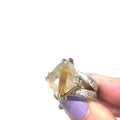 Close-up of Rutilated Quartz showing golden Rutile inclusions within clear quartz on white in finger tips for close up view