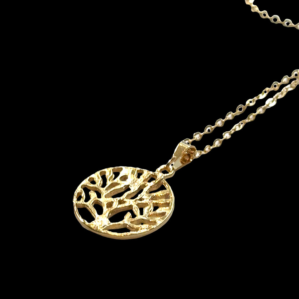 Close-up of Tree of Life pendant showing detailed branch work and circular design, on a Black background laying flat on a 18'' gold filled chain, front view. 