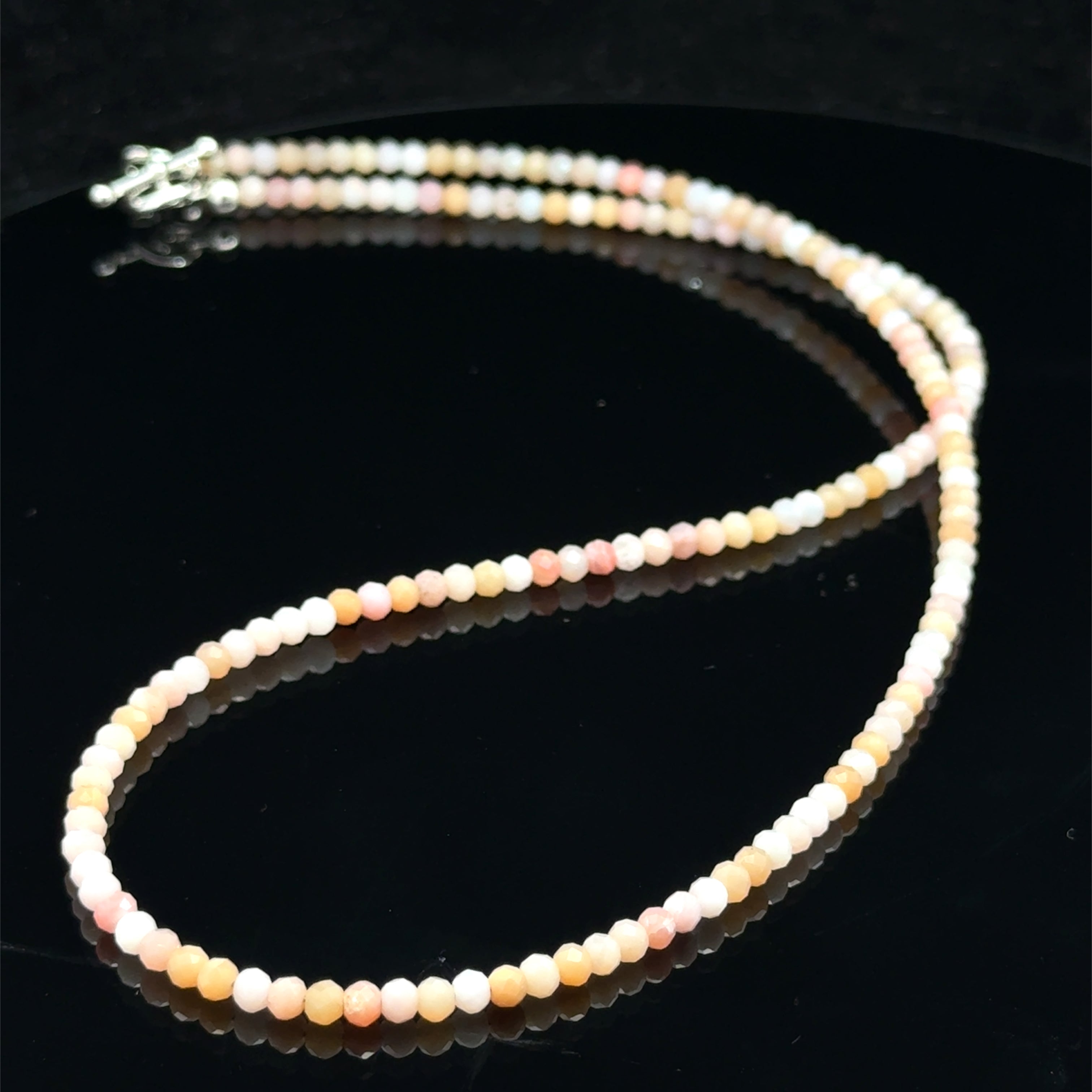 Close-up of faceted pink opal gemstone beads catching light on delicate beaded necklace on a black background, front view. 
