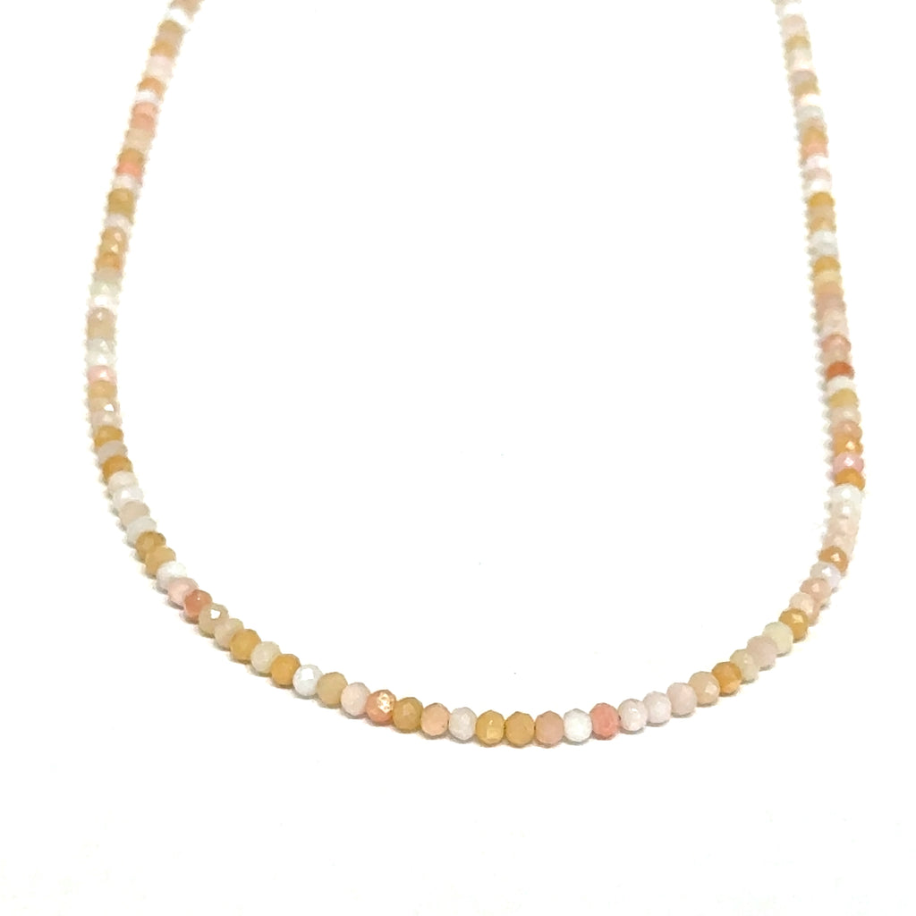 Close-up of faceted pink opal gemstone beads catching light on delicate beaded necklace on a white background, front hanging view.